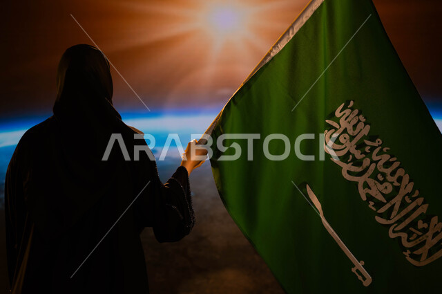 التباهي والتفاخر بإنجازات الوطن، اليوم الوطني السعودي، الاحتفال بيوم العلم 11 مارس، صورة من الخلف لامرأة سعودية عربية خليجية محجبة تحمل العلم السعودي، النظر الى كوكب الأرض وقت غروب الشمس، العيد الوطني السعودي 8 ربيع الأول، رحلة السعودية للفضاء الخارجي