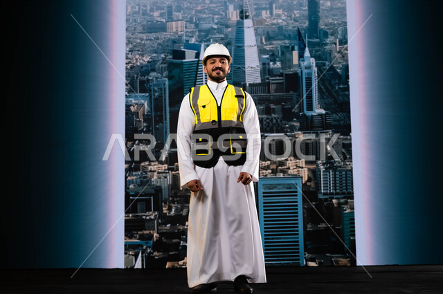 وظائف ومهن سعودية, الأبراج و الإنجازات العمرانية في الرياض التي تحققت بفضل مهندسي الوطن, إيماءات الافتخار بالنهضة العمرانية للمملكة, مشاريع هندسية تنموية وطنية سعودية, مهندس عربي سعودي خليجي مبتسم يرتدي الخوذة وسترة الحماية يقف بشموخ, خلفية أبراج الرياض