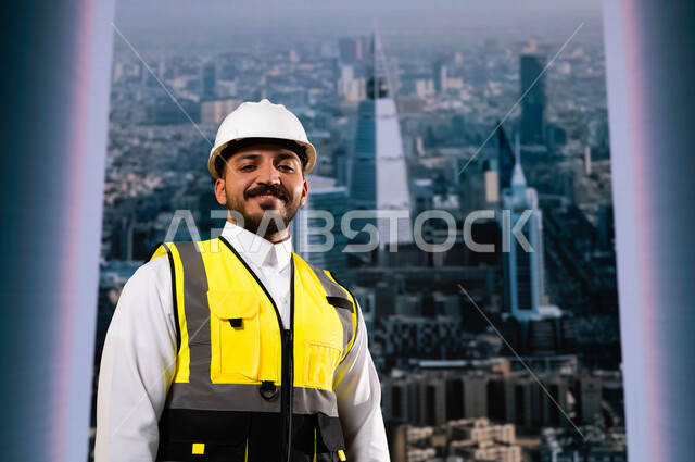 مشاريع هندسية تنموية وطنية سعودية, الأبراج و الإنجازات العمرانية في الرياض التي تحققت بفضل مهندسي الوطن, إيماءات الافتخار بالنهضة العمرانية للمملكة, صورة مقربة لمهندس عربي سعودي خليجي مبتسم يرتدي الخوذة وسترة الحماية يقف بشموخ, خلفية أبراج الرياض