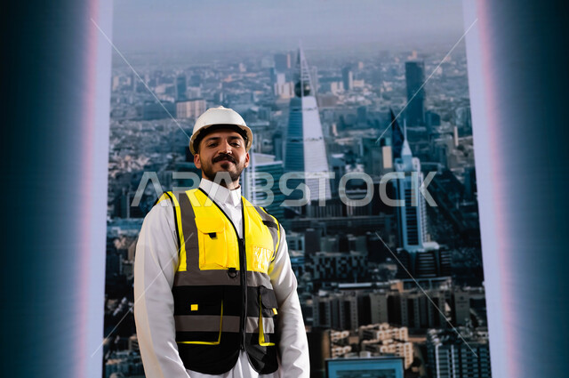 الأبراج و الإنجازات العمرانية في الرياض التي تحققت بفضل مهندسي الوطن, إيماءات الافتخار بالنهضة العمرانية للمملكة, مشاريع هندسية تنموية وطنية سعودية, مهندس عربي سعودي خليجي مبتسم يرتدي الخوذة وسترة الحماية يقف بشموخ, وظائف ومهن سعودية, خلفية أبراج الرياض