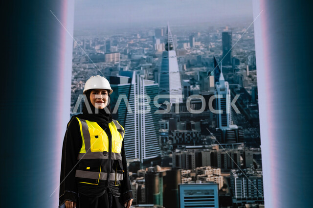 إيماءات الافتخار و الاعتزاز بالنهضة العمرانية للمملكة, مشاريع إعمارية سعودية وطنية, مهندسة عربية سعودية خليجية محجبة ترتدي الخوذة وسترة الحماية تقف بشموخ, بناء الوطن بسواعد أبنائه ومهندسيه, التطور العمراني المتميز للرياض, خلفية أبراج الرياض