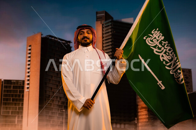 الاحتفال باليوم الوطني السعودي، تجديد الذكرى التاريخية لتوحيد المملكة 23 سبتمبر، يوم العلم 11مارس، تنمية روح الانتماء للوطن، رجل عربي سعودي خليجي يرتدي الشماغ والثوب التقليدي ويحمل علم السعودية، العيد الوطني السعودي، خلفية مركز الملك عبد الله المالي