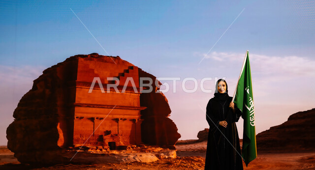 إحياء إرث الأجداد والاعتزاز بإنجازاتهم، أعياد ومناسبات وطنية سعودية، الاحتفال باليوم الوطني 8 ربيع الأول، العيد الوطني السعودي، يوم العلم 11 مارس، إمرأة عربية سعودية خليجية مبتسمة ترتدي العباءة السوداء وتحمل علم المملكة، خلفية قصر الفريد التاريخي في العلا