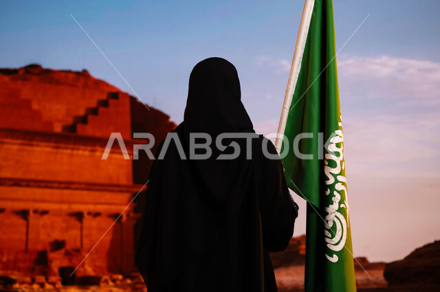 The identity of the Saudi National Day 93, the celebration of Flag Day 2023, the anniversary of the National Day September 23, a back image of a Saudi Arabian Gulf woman wearing a black abaya and holding the kingdom's flag, reviving the history of the anc