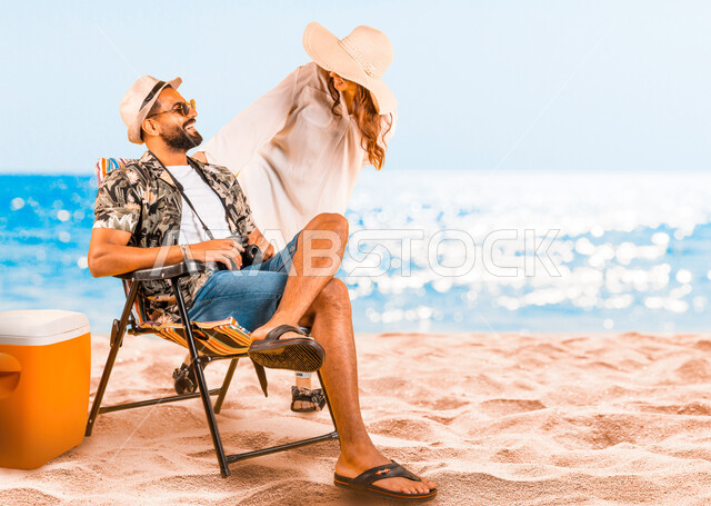 تبادل الدردشات والضحك والتسامر مع الزوجة بإيماءات السرور، قضاء أوقات الفراغ في العطله الصيفيه أمام البحر، شاب عربي خليجي سعودي يرتدي الزي الكاجوال والنظارة الشمسية يجلس على الكرسي على الشاطئ في المناطق الساحليه، الترفيه عن النفس بالسياحة والسفر