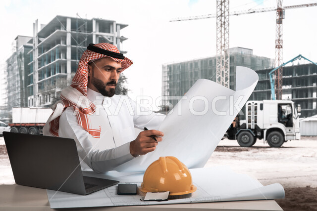 إدارة المشاريع الهندسية باستخدام جهاز الحاسوب المحمول، استخدام التقنيات الحديثة لتدقيق وتقييم المخططات والتصاميم المعمارية ،مهندس عربي خليجي سعودي يرتدي الثوب التقليدي ويجلس في ،موقع العمل، متابعة سير المشاريع الإعمارية, مهن ووظائف سعودية