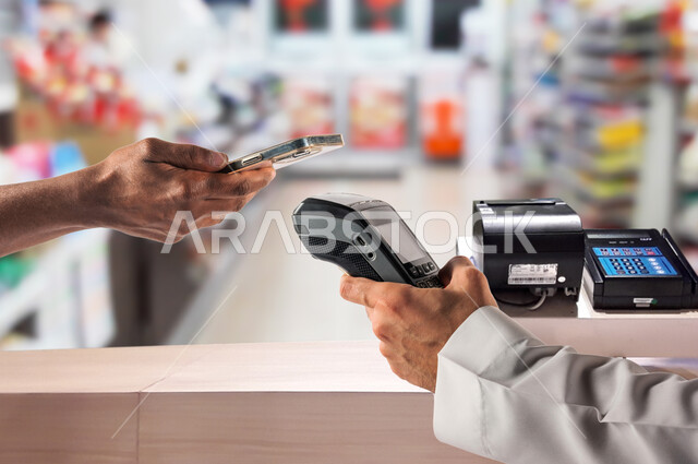 The use of modern methods and technologies in electronic payment, the ease of automatic payment in food stores in Saudi Arabia, a close-up photo of a Saudi Gulf Arab man paying the account via mobile phone at the cashier, shopping for some household needs and supplies.