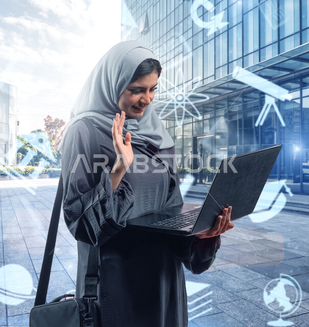 متابعة المحاضرات الدراسيه عبر الانترنت، الوقوف أمام مبنى الجامعه، طالبه جامعيه عربيه خليجية سعودية محجبة ترتدي العباءة وتقوم بإجراء مكالمة فيديو عبر جهاز الحاسوب المحمول، ايقونات علمية لمجالات التعليم المختلفه بتقنية هولوجرامية، الدراسه عن بعد عن طريق الاونلاين