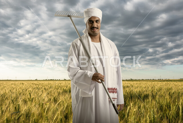 أراضي زراعيه خضراء، أدوات ومعدات الزراعة، فلاح مصري يرتدي الزي المصري التقليدي ويحمل بيده مشط الارض والحدائق (المدمة)، الوقوف في حقول الارز، استقدام العمالة من الخارج، النظر إلى الكاميرا بإيماءات السعادة، منظر السماء الملبدة بالغيوم