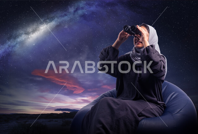 التخطيط المستقبلي للأهداف و الطموحات، رؤية الاشياء البعيدة و حب الاستكشاف والمغامرة، حب الاستكشاف والمغامرة، صورة مقربة من الخلف لسيدة عربية خليجية سعودية محجبة تجلس على كرسي مريح وتنظر من خلال المنظار , خلفية السماء المرصعه بالنجوم