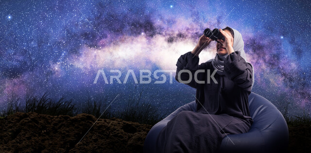 التخطيط المستقبلي للأهداف و الطموحات، رؤية الاشياء البعيدة و حب الاستكشاف والمغامرة، حب الاستكشاف والمغامرة، صورة مقربة من الخلف لسيدة عربية خليجية سعودية محجبة تجلس على كرسي مريح وتنظر من خلال المنظار , خلفية السماء المرصعه بالنجوم