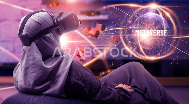 قضاء أوقات ممتعه في مشاهدة البرامج الترفيهيه في العطلة الصيفيه، صورة مقربة من الخلف لسيدة عربيه خليجية سعودية محجبة ترتدي العباءة الخليجيه ونظارة الواقع الافتراضي وتجلس على كرسي مريح ، خلفيه هولوجراميه ثلاثية الابعاد لافلام والعاب الواقع الافتراضي