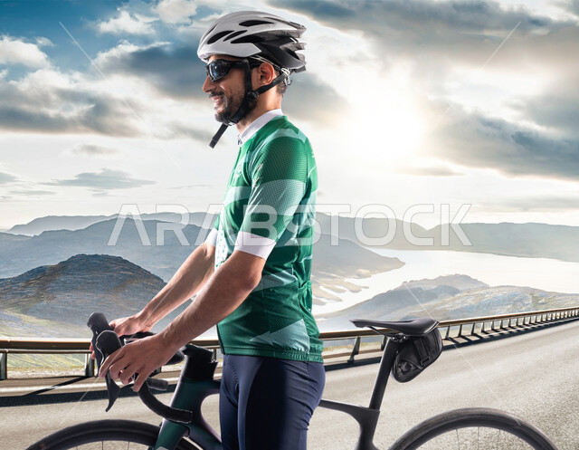 نشاط بدني للمحافظه على الصحه و اللياقه الجسديه, ممارسة هواية ركوب الدراجة، شاب عربي خليجي سعودي يرتدي زي الرياضة الخاص بسباق الدراجات الهوائية ، الاستعداد لبدء المسابقة بإيماءات السعادة، خلفية الطبيعه الجبلية