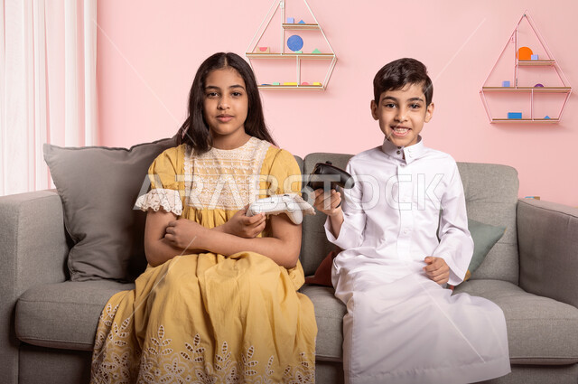 مفهوم الفوز والخسارة، ولدان عربيان خليجيان سعوديان يحملان عصا التحكم يستمتعان باللعب في ألعاب الفيديو في العطلة الصيفيه، الاستمتاع في اوقات الفراغ، التحدي والمغامرة والتنافس، تقنيات وألعاب حديثة متطورة، ايماءات تدل على الربح والانتصار