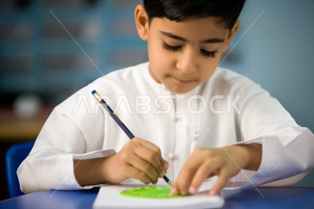 The skill of concentration and innovation using engineering tools, a close-up of an Arab Gulf Emirati preparatory student wearing casual clothes learning geometric shapes and how to draw them, the development of educational means in the Emirates, enjoying