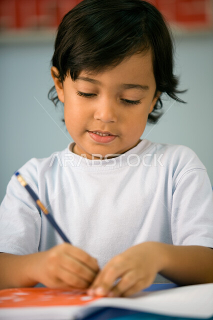 استخدام الأدوات الهندسية وتنمية مهارة الابتكار، صورة مقربة لطالب تمهيدي عربي خليجي إماراتي يرتدي الزي الكاجوال يتعلم الأشكال الهندسية وطريقة رسمها, تطور وسائل التعليم في الإمارات، الاستمتاع بالنشاطات الترفيهيه داخل الفصل الدراسي