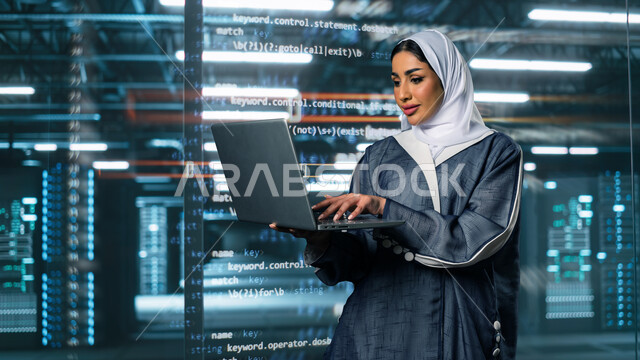 إستثمار الخبرات السعودية في بناء مراكز بيانات متطورة وحديثة، مفهوم  تكنولوجيا التخزين السحابي, صورة مقربة لامرأة عربية خليجية سعودية تستخدم اللابتوب في الإشراف وإدارة معلومات الداتا سنتر, خلفية هولوجرامية لأكواد البرمجة داخل غرفة التحكم بالسيرفرات وخوادم الانترنت