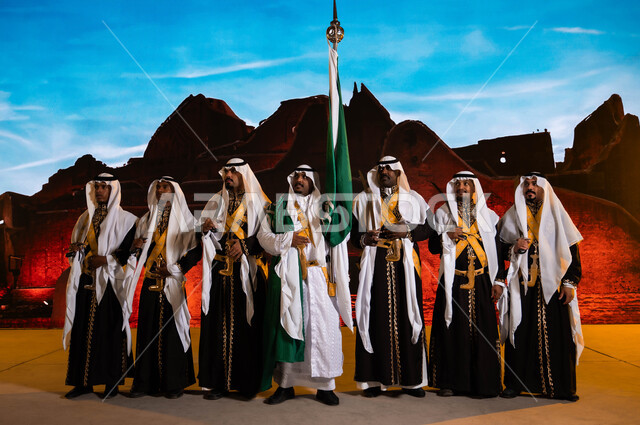 يوم العلم السعودي 11 مارس، الوقوف أمام قصر سلوى في الدرعية، مناسبات وطنية تقليدية في 23 سبتمبر، فرقة العرضة الحجازية تنظر إلى شيء ما، الفلكلور الشعبي السعودي، ارتداء الدقلة والفرميلة التراثية، الاحتفال بذكرى اليوم الوطني، مفهوم حب الوطن و الانتماء إليه