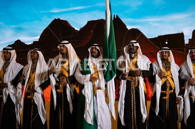 Saudi popular folklore, the background of Salwa Palace in Diriyah, traditional national occasions on Rabi’ al-Awwal 8, the Hijazi Ardha band looking at something, wearing the traditional daqla and bra, Saudi Flag Day March 11, celebrating the anniversary of the National Day, strengthening the Queen’s national identity