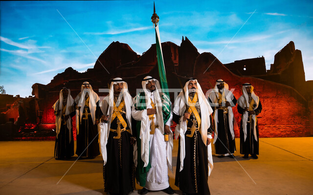 Celebrating Saudi Flag Day, March 11, preparing for celebrations and chants, commemorating National Day, September 23, costumes for celebrations and national occasions, Saudi traditional folklore arts and performances, wearing the popular daqla and bramila, a close-up of the Hijazi Ardha band and looking at something