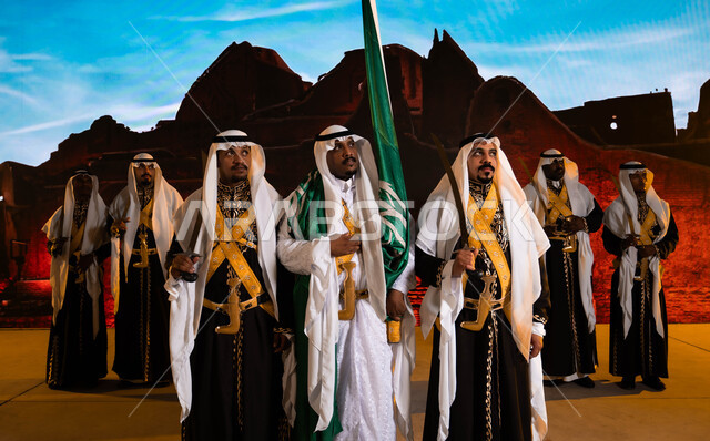 Preparing for songs and celebrations, commemorating the Saudi National Day, Rabi’ al-Awwal 8, costumes for traditional national occasions, Saudi traditional folklore arts and performances, wearing the popular daqla and veil, Saudi Flag Day, March 11, a close-up of the Hijazi Ardha band and looking at something.