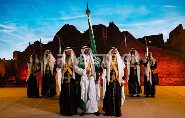 Preparing for celebrations and chants, commemorating the Saudi National Day, Rabi’ al-Awwal 8, costumes for traditional national occasions, Saudi traditional folklore arts and performances, wearing the popular dahla and veil, celebrating Saudi Flag Day, March 11, a close-up of the Hijazi Ardha band and looking at something.