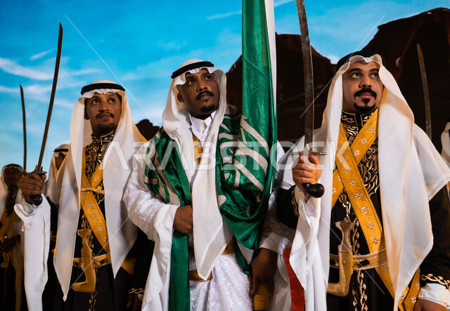 Traditional national occasions, the background of Salwa Palace in Diriyah in Riyadh, Saudi folklore, wearing the traditional dhokla and bra, Saudi Flag Day, March 11, celebrating the anniversary of National Day, March 23, the Hijazi Ardha band, songs, and folk dance, looking at something