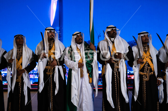 Strengthening the national spirit, a close-up photo of the Hejazi Ardha band wearing the popular Dhakla and Vermeilah costume, popular activities on national occasions, the anniversary of the Eid and the Saudi National Day on September 23, the celebration of the Saudi Flag Day on March 11, the background of the Kingdom Tower and skyscrapers.