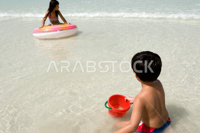 الإستمتاع بالفعاليات الصيفية الممتعة مع الأخوة, أخوان عربيان إمراتيان خليجيان يقومان باللعب على شاطئ البحر في رحلة صيفية, أنشطة ترفيهية عائلية في العطلة, منتجعات شاطئية في الإمارات