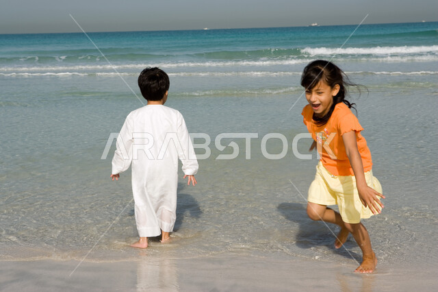 التسلية والترفيه بالفعاليات الصيفية الممتعة مع الأخوة, أخوان عربيان إمراتيان خليجيان يقومان باللعب على شاطئ البحر في رحلة صيفية, أنشطة ترفيهية عائلية في العطلة، منتجعات شاطئية في الامارات