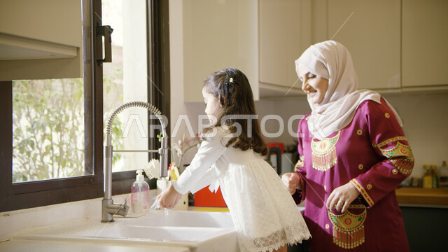 Washing hands with soap and water, maintaining personal hygiene, spending quality time with children, enjoying doing housework with the daughter, helping to clean and wash dishes, raising children to love cooperation, a close-up of an Arab Gulf Emirati mo