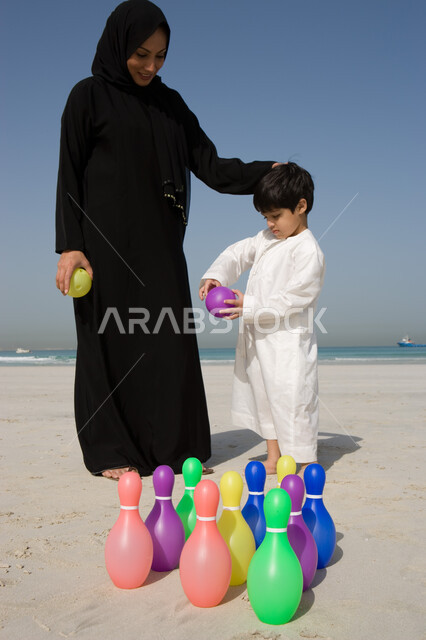 السرور والسعادة بقضاء الوقت في إسعاد الإبن، مفهوم الأمومة وحب الأبناء، أم عربية خليجية إماراتية محجبة تضع يدها على رأس ولدها بإيماءات العطف والحنان وتشاركه باللعب ، استخدام دبابيس البولينج البلاستيكية في اللعب، الأنشطة الترفيهية المختلفة للأطفال