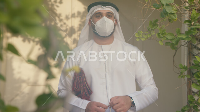 الاستعداد للذهاب وتأدية الصلوات على وقتها في المسجد، التقرب الى الله بالتسبيح والأذكار اليومية، صورة مقربة لرجل عربي خليجي اماراتي يرتدي الكندورة والغترة يحمل بيده سجادة الصلاة، الالتزام بالاجراءات الاحترازية وارتداء الكمامة للوقاية من فايروس كورونا.