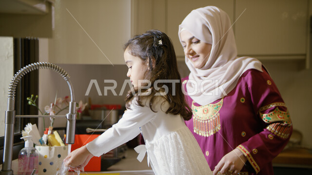 الإستمتاع بأداء الأعمال المنزليه برفقة الأبناء، المساعده في تنظيف وغسيل الأطباق، تربيه الأطفال على حب التعاون، صورة مقربة لأم عربية خليجية اماراتية تقف مع ابنتها في المطبخ، غسل اليدين بالماء والصابون والمحافظة على النظافه الشخصية.