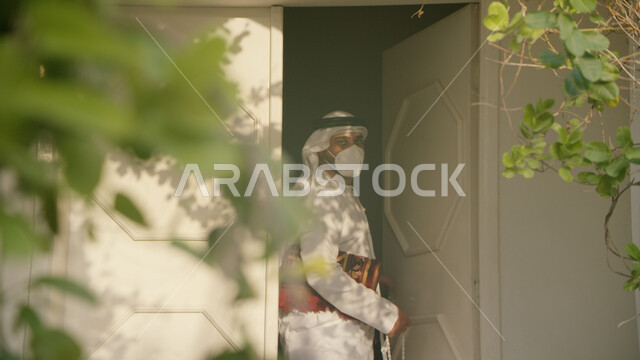 أداء الفرائض الدينية، الاستعداد للذهاب إلى المسجد و أداء الصلوات على وقتها ،اسلاميات وعبادة، صورة مقربة لرجل عربي خليجي اماراتي يرتدي الكندورة والغترة يحمل بيده سجادة الصلاة، الالتزام بالاجراءات الاحترازية وارتداء الكمامة للوقاية من فايروس كورونا.