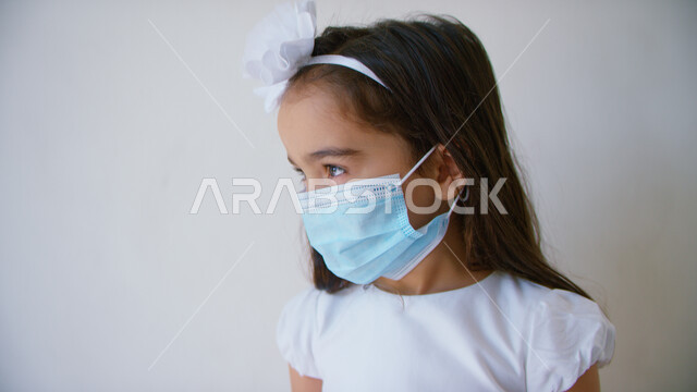 الوعي الصحي وتجنب إنتشار العدوى، مفهوم إتباع الإجراءات الوقائيه لضمان السلامة من فايروس كورونا، بورتريه مقرب لفتاة عربيه خليجيه اماراتية ترتدي فستان أبيض وتضع الكمامة للحمايه من الإصابه بكوفيد-١٩، ايماءات النظر إلى شيء ما، خلفيه بيضاء.