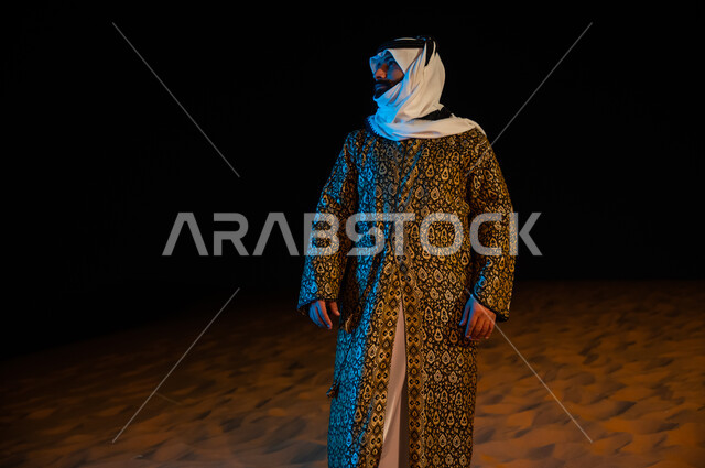 Standing with confidence and pride, contemplating and looking at something, the soft golden sands in the desert environment, a Saudi Arab Gulf man wearing the traditional dagger and ghutra standing in the desert of the Kingdom of Saudi Arabia, nature back