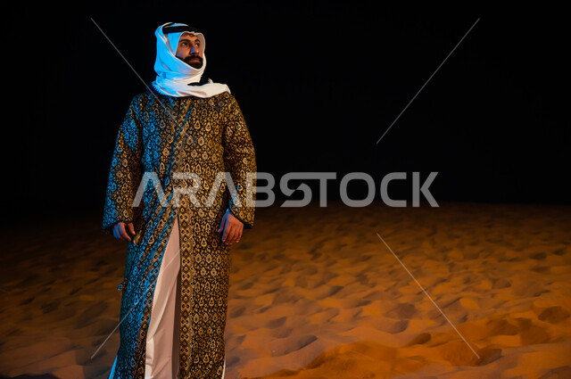 التامل والنظر الى شيء ما، الرمال الذهبية الناعمة في البيئة الصحراوية، رجل عربي خليجي سعودي ير تدي الدقله والغتره الشعبيه التقليديه ويقف في صحراء المملكة العربية السعودية، صورة الجسم بالطول الكامل ، الوقوف بثقة واعتزاز، خلفية الطبيعة