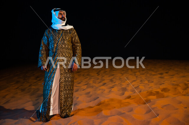 الرمال الذهبية الناعمة في البيئة الصحراوية، رجل عربي خليجي سعودي ير تدي الدقله والغتره الشعبيه التقليديه ويقف في صحراء المملكة العربية السعودية، صورة الجسم بالطول الكامل ، الوقوف بثقة واعتزاز، التامل والنظر الى شيء ما، خلفية الطبيعة