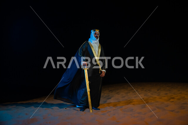 الحفاظ على السلامة  والأمن، رجل عربي خليجي سعودي يرتدي الغتره والبشت ويحمل بيده سيف في الخارج وقت الليل، الوقوف باعتزاز وثقة بدولة السعودية, التامل والنظر الى شيء ما, خلفية الطبيعه الصحراوية، صورة الجسم بالطول الكامل