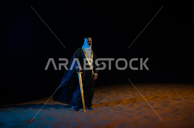 الحفاظ على الامن والسلامة ، رجل عربي خليجي سعودي يرتدي الغتره والبشت ويحمل بيده سيف في الخارج وقت الليل، الوقوف باعتزاز وثقة بدولة السعودية, التامل والنظر الى شيء ما, خلفية الطبيعه الصحراوية، صورة الجسم بالطول الكامل