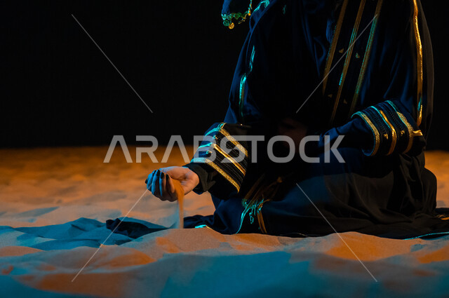 خلفية الرمال الذهبية الناعمة، الاعتزاز والفخر الدائم بالهوية الوطنية السعودية, مشاعر الحب والانتماء للبلاد, مفهوم حب الوطن والانتماء إليه, صورة مقربة ليد امرأة عربيه خليجية ترتدي عباءة سوداء و تمسك تراب الوطن افتخارا بأصولها و جذورها