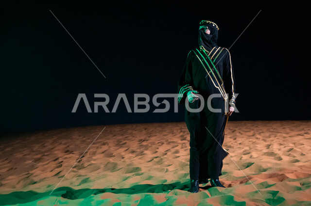ذكرى يوم التاسيس السعودي 22 فبراير، انعكاس ضوء أخضر على الرمال الذهبية، التأمل والنظر إلى شيء ما، امرأه سعودية ترتدي العباءة السعودية والبرقع تقف في الصحراء  بثقة واعتزاز بالدولة السعودية، صورة الجسم بالطول الكامل، ارتداء أزياء يوم التأسيس السعودي1727 م