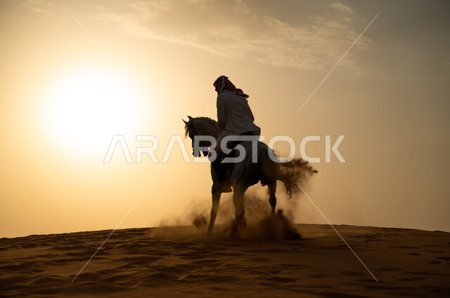 اتباع تقاليد الأجداد برعاية وتربية الجياد والاهتمام بها، حب وعشق الخيل السعودي الأصيل، رجل عربي خليجي سعودي يرتدي الشماغ والزي التقليدي يمتطي فرسه وقت غروب الشمس، التجول في الطبيعة الصحراوية على ظهر الحصان، أنشطة وفعاليات ركوب الأحصنة في الصحراء.