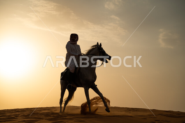 اتباع تقاليد الأجداد برعاية وتربية الجياد والاهتمام بها، حب وعشق الخيل السعودي الأصيل، رجل عربي خليجي سعودي يرتدي الشماغ والزي التقليدي يمتطي فرسه وقت غروب الشمس، التجول في الطبيعة الصحراوية على ظهر الحصان، أنشطة وفعاليات ركوب الأحصنة في الصحراء.