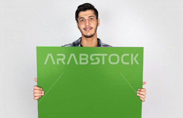 بورتريه رجل سعودي يمسك لوحة خضراء كبيرة فارغة ، يرتدي  لباس كاجوال ، بخلفية بيضاء