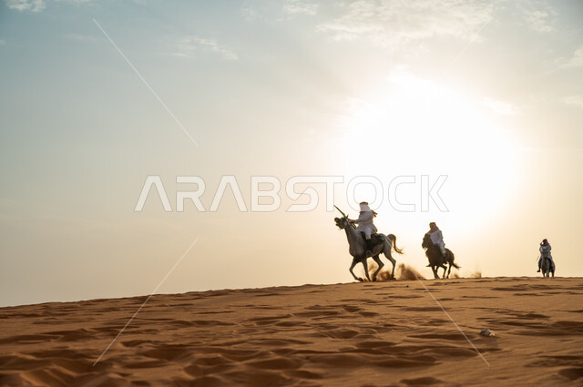 أنشطة وفعاليات ركوب الجياد في الصحراء، ذكرى اليوم الوطني السعودي 23 سبتمبر، رفع الراية للاحتفال بيوم العلم السعودي 11 مارس، مجموعة رجال عرب خليجيون سعوديون يتجولون على ظهر الاحصنة وقت غروب الشمس، حب وعشق الخيل السعودي الأصيل
