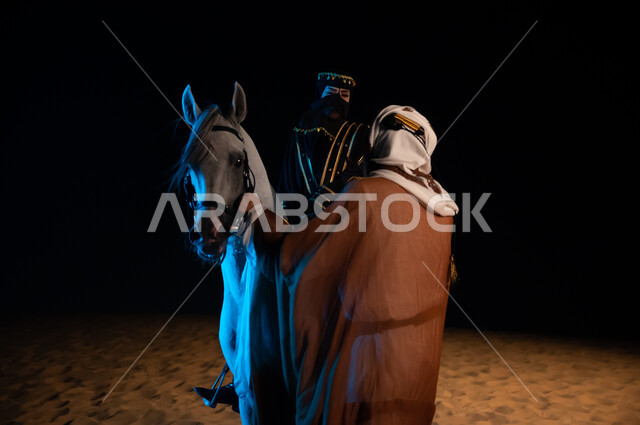 تبادل الأحاديث الجانبية المسلية، الشغف في تربية الحيوانات الأليفة، ذكرى يوم التاسيس السعودي 22 فبراير، إمرأة ورجل خليجيان سعوديان يرتديان ازياء يوم التأسيس السعودي1727 م و يتبادلان الدردشات والحوارات الوديه في الصحراء ليلا، خلفية الطبيعه الرملية الذهبية