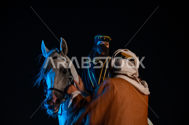 The memory of the Saudi founding day, February 22, practicing the hobby of riding horses, chatting and friendly dialogues, a close-up of a Saudi Arabian Gulf woman and man wearing the clothes of the Saudi founding day 1727 AD and exchanging entertaining s