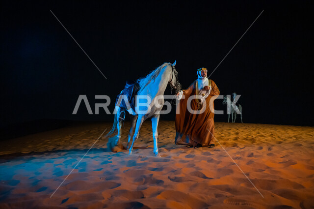 Participation of horses in national holidays and events, wandering in the soft golden sandy nature, wearing the costumes of the people of the central region, a Saudi man wearing the costume of the founding day 1727 AD standing next to his horse in the desert, the anniversary of the founding of the Kingdom February 22, full-length body photo